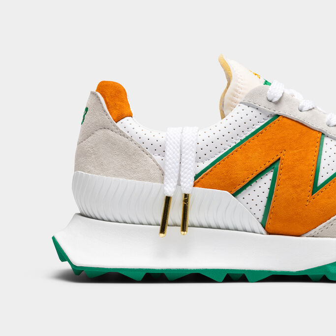 Side profile of the orange and green XC-72 sneaker with a pair of laces hanging out of the collar showing the gold endcaps.