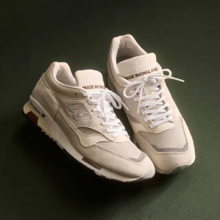 A pair of New Balance Made in UK sneakers on a green textured studio environment. 