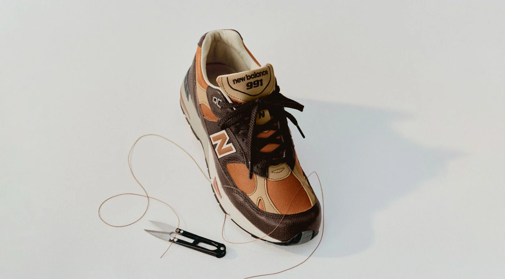 A New Balance Made in UK sneaker in a white studio environment next to sewing thread and fabric shears. 