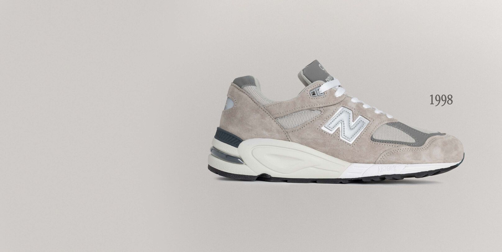 A grey 990v1 sneaker sitting on a grey background.