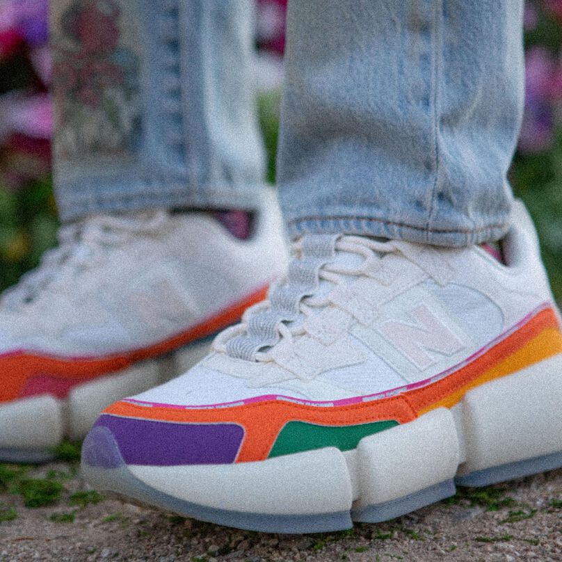 Knee down shot of a person wearing a pair of white Vision Racers with multiple color accents.
