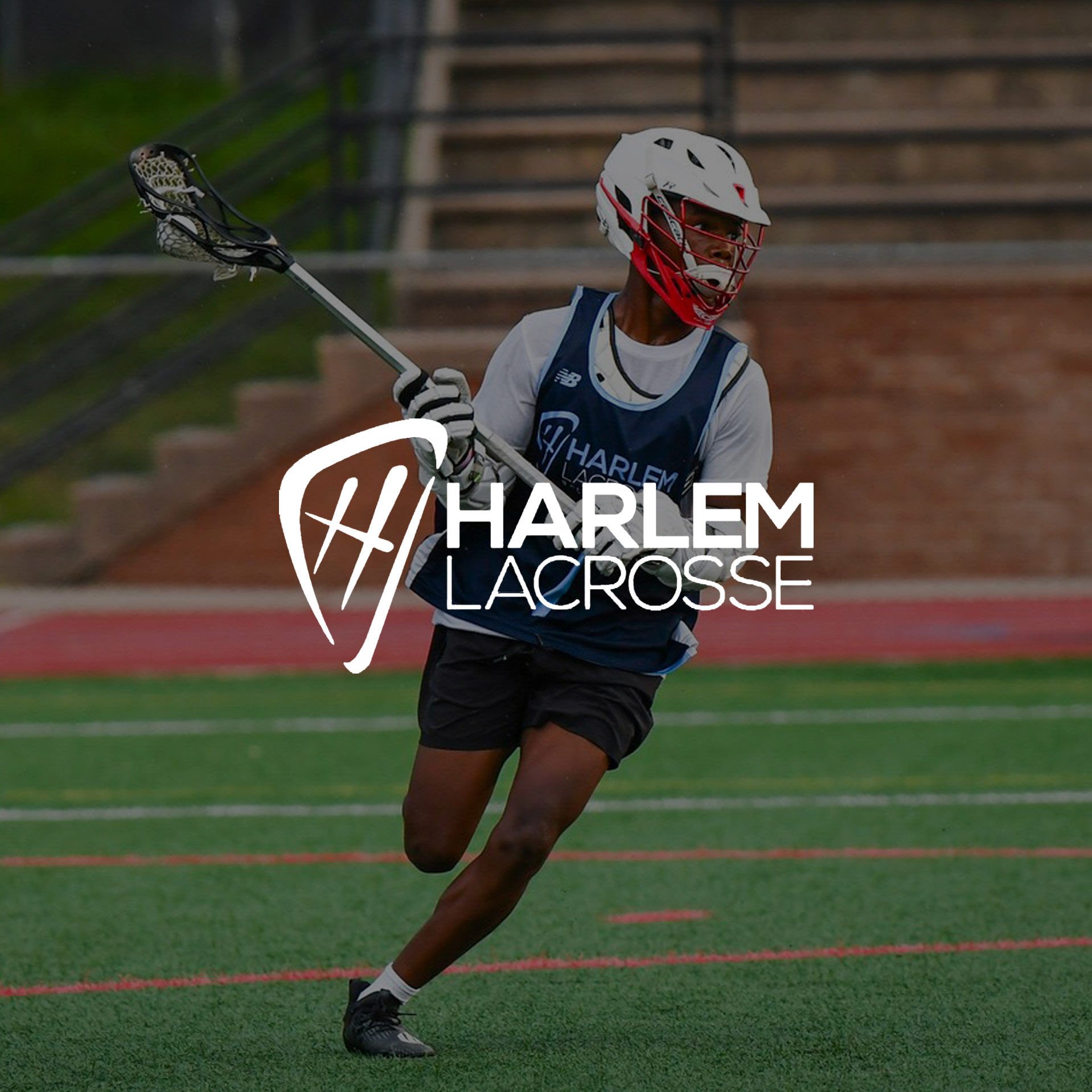 A dark-skinned, uniformed teen male-presenting student athlete running down the field holding a lacrosse stick.