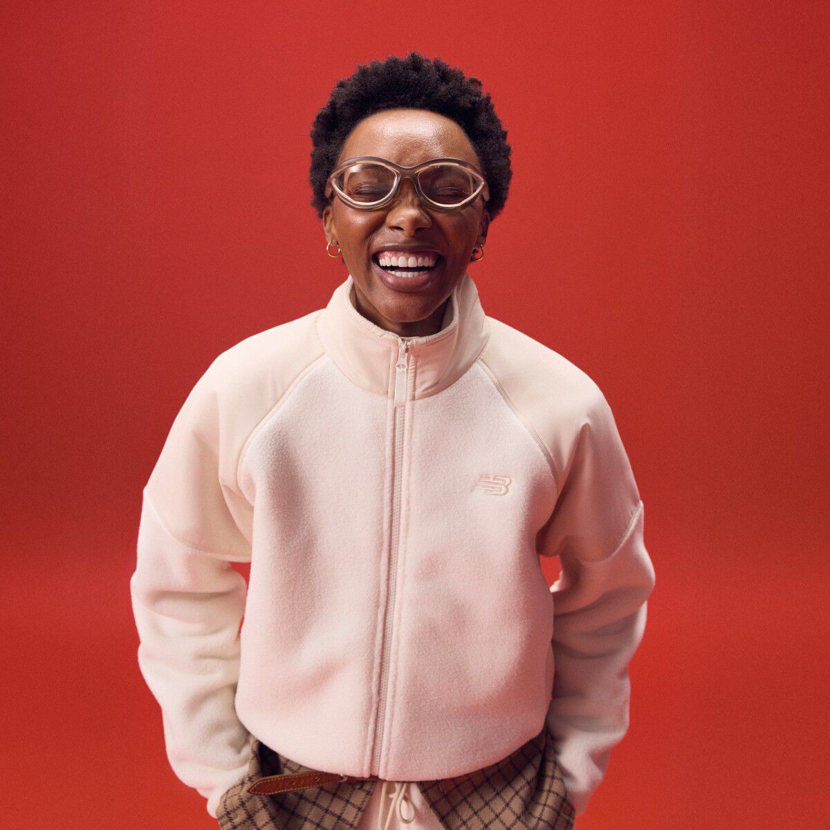Woman laughing while wearing a pink zip-up on a red background.