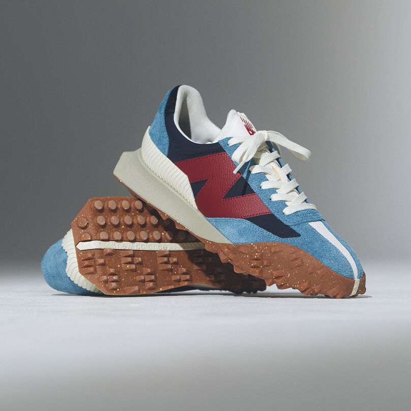 Pair of blue and red shoes proped on top of each other on a grey background.