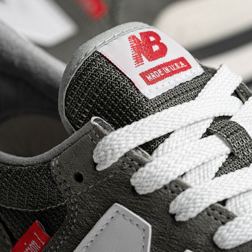 Detail crop of the tongue and upper of a grey NB 990 Version 1 sneaker accented with red labels