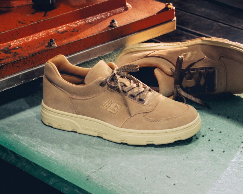Knee down view of a man wearing a pair of New Balance Made in UK sneakers standing on a patterned tile floor.  